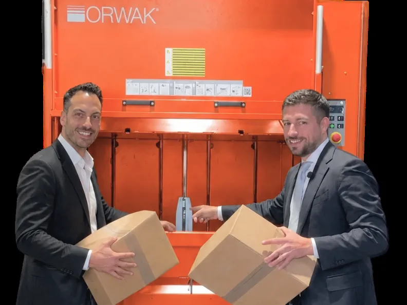 Marc Schleibaum von BEMA und Angelo Di Vita mit Kartons vor einer ORWAK Ballenpresse